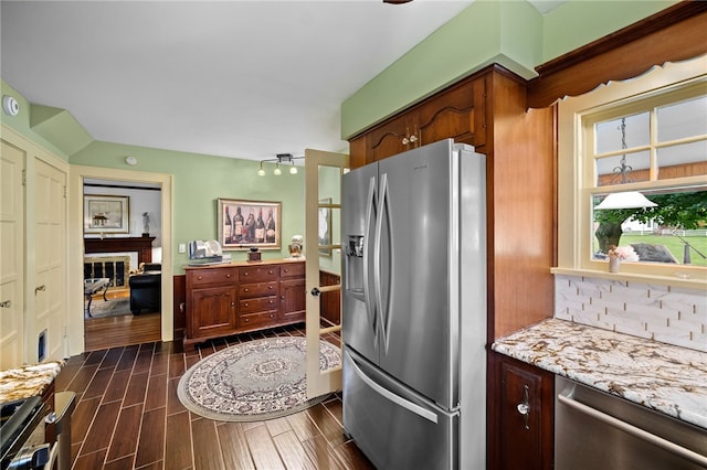 kitchen featuring light stone counters, wood tiled floor, stainless steel appliances, a brick fireplace, and backsplash