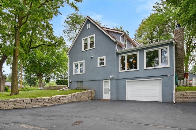 view of side of home featuring a garage, a yard, driveway, stucco siding, and a chimney