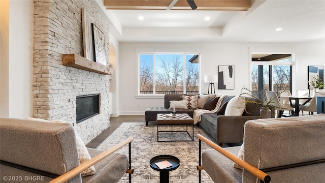 living area with recessed lighting, dark wood-style flooring, a stone fireplace, and baseboards