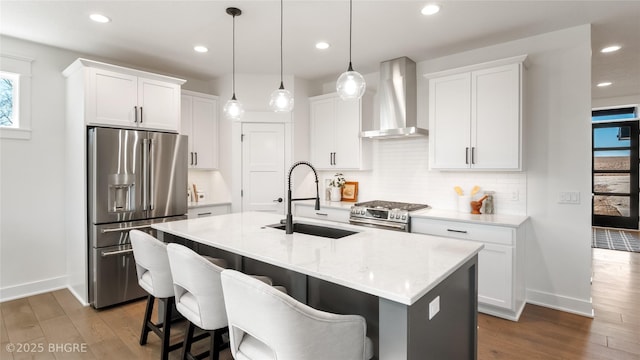 kitchen with dark wood-style flooring, stainless steel appliances, tasteful backsplash, a sink, and wall chimney range hood