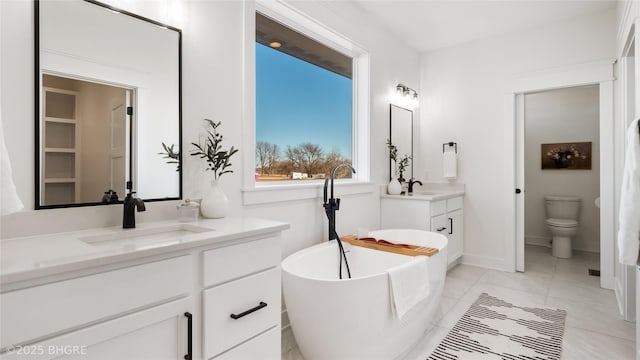 bathroom with a freestanding tub, two vanities, a sink, and toilet