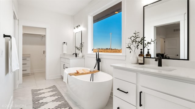 full bath with a walk in closet, a soaking tub, two vanities, visible vents, and a sink