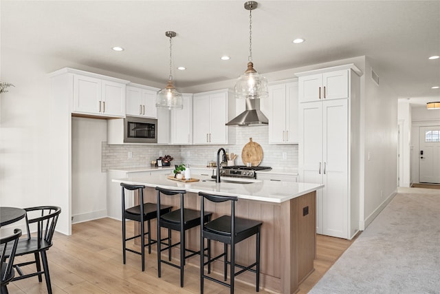 kitchen featuring a center island with sink, wall chimney exhaust hood, white cabinetry, and built in microwave