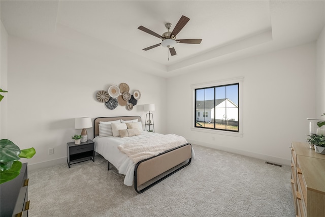 bedroom with light carpet, a raised ceiling, and ceiling fan