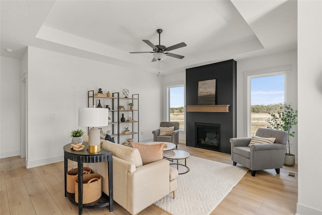 living room featuring ceiling fan, light hardwood / wood-style flooring, a fireplace, and a tray ceiling