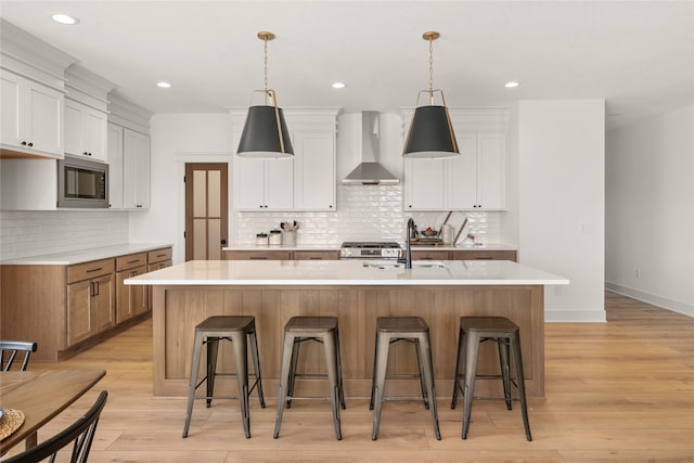 kitchen with white cabinets, a large island, and wall chimney range hood