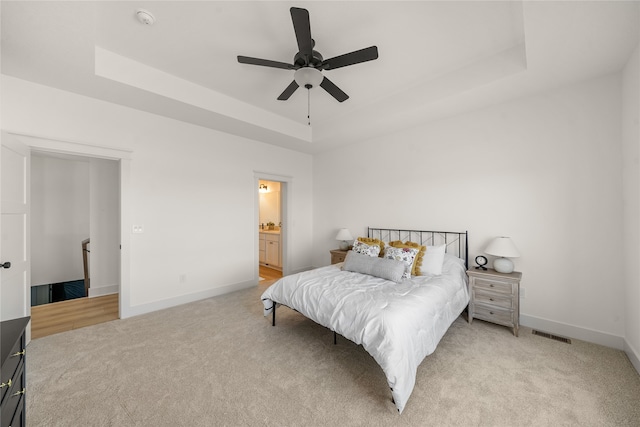 carpeted bedroom with ceiling fan, ensuite bath, and a tray ceiling