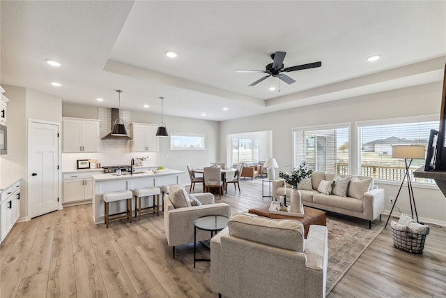 living room featuring ceiling fan, sink, light hardwood / wood-style floors, and a tray ceiling