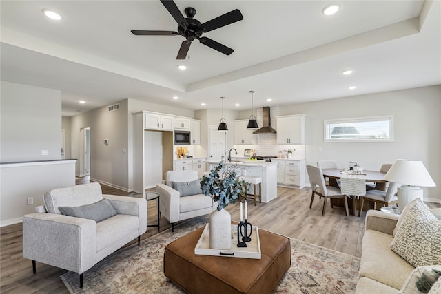 living room with ceiling fan, a raised ceiling, and light hardwood / wood-style flooring