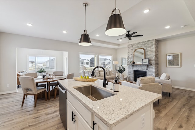 kitchen featuring decorative light fixtures, sink, a kitchen island with sink, light stone counters, and a raised ceiling