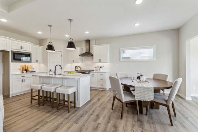 kitchen featuring white cabinetry, decorative light fixtures, black microwave, and wall chimney exhaust hood