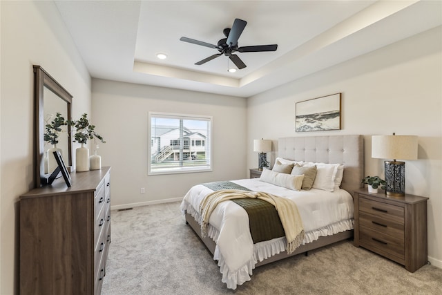 bedroom featuring light carpet, a tray ceiling, and ceiling fan