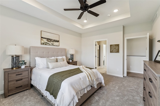 carpeted bedroom with a raised ceiling and ceiling fan