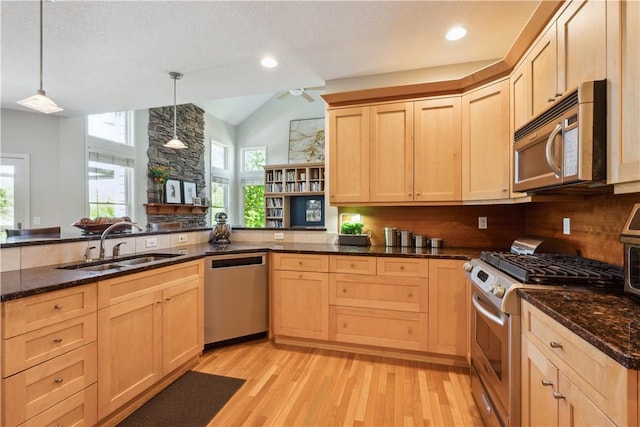 kitchen featuring kitchen peninsula, appliances with stainless steel finishes, light brown cabinetry, hanging light fixtures, and sink