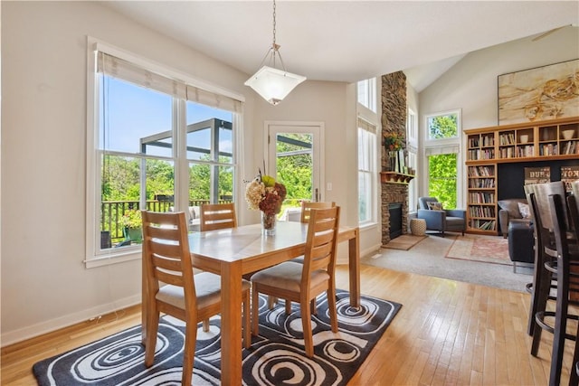 dining area with light wood-type flooring, a fireplace, and vaulted ceiling