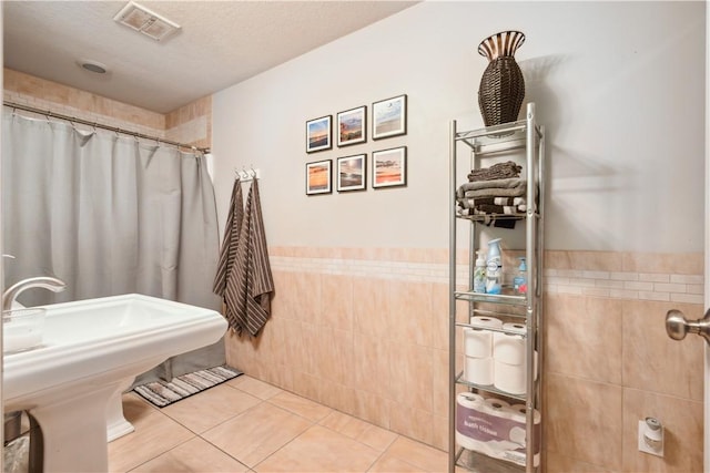 bathroom featuring a textured ceiling, tile patterned flooring, tile walls, and curtained shower