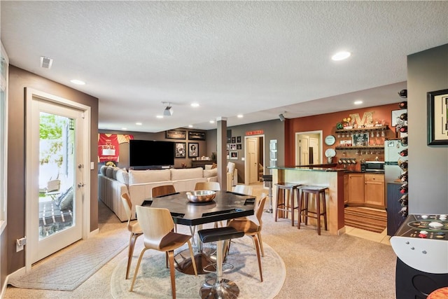 dining room featuring light colored carpet, indoor bar, and a textured ceiling