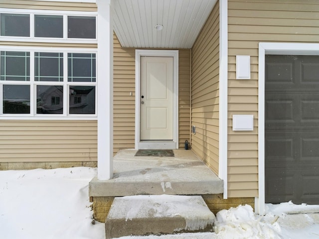 snow covered property entrance featuring a garage