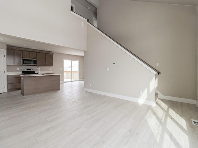 unfurnished living room with light wood finished floors, stairway, a high ceiling, a sink, and baseboards