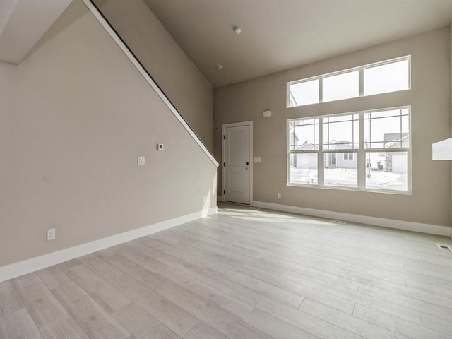 unfurnished living room featuring visible vents, light wood finished floors, a towering ceiling, and baseboards