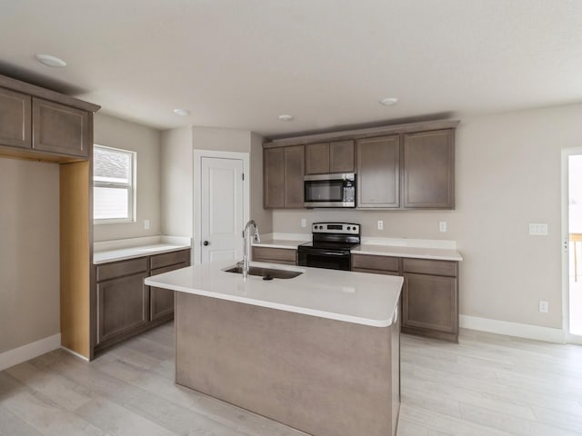 kitchen featuring range with electric stovetop, a center island with sink, light countertops, stainless steel microwave, and a sink