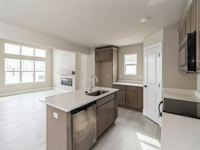 kitchen with a glass covered fireplace, an island with sink, light countertops, stainless steel dishwasher, and a sink