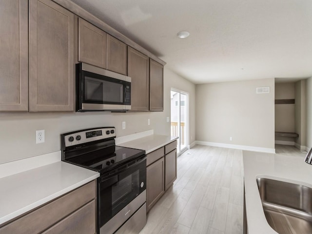 kitchen with baseboards, appliances with stainless steel finishes, light countertops, light wood-type flooring, and a sink