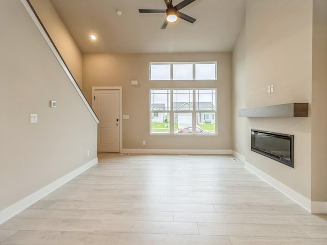 unfurnished living room with a ceiling fan, baseboards, a glass covered fireplace, recessed lighting, and light wood-style flooring