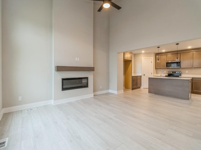 living room with a ceiling fan, a glass covered fireplace, a towering ceiling, and light wood finished floors