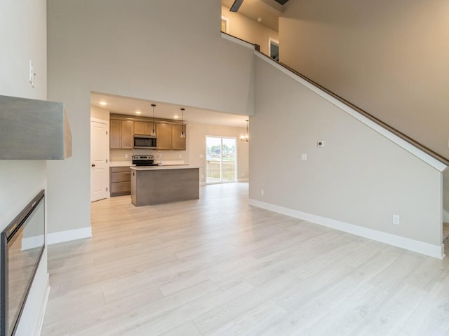 unfurnished living room with baseboards, a notable chandelier, light wood-style flooring, and a towering ceiling