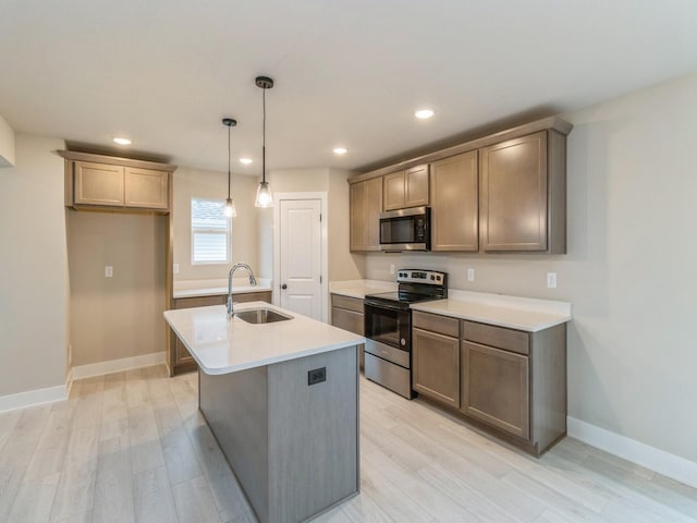 kitchen featuring light wood-style floors, a center island with sink, light countertops, a sink, and appliances with stainless steel finishes
