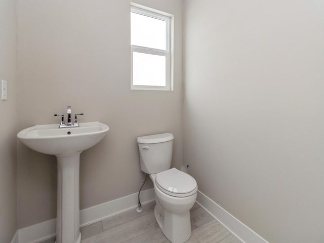 half bathroom with toilet, baseboards, and a sink