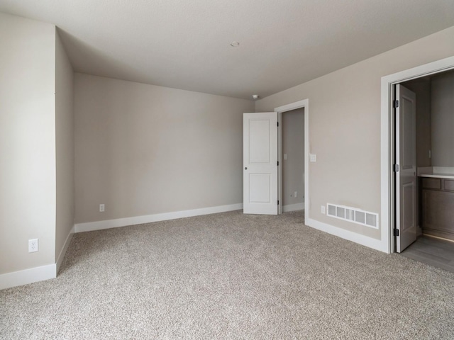 unfurnished bedroom featuring baseboards, ensuite bathroom, light colored carpet, and visible vents