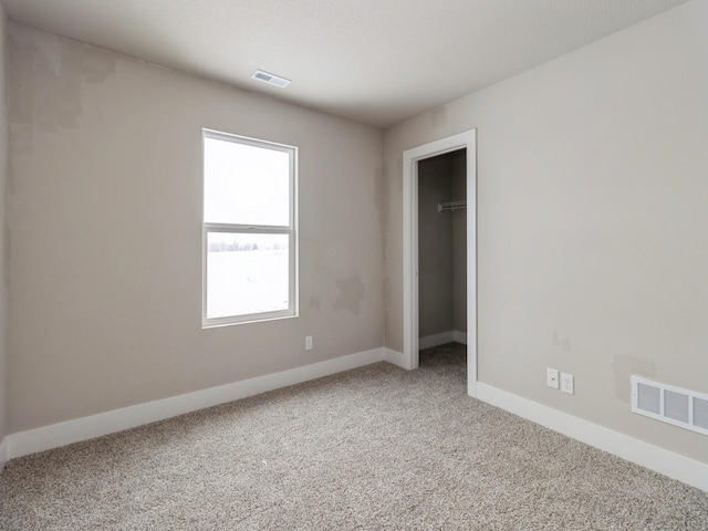 unfurnished bedroom featuring baseboards, light carpet, a spacious closet, and visible vents