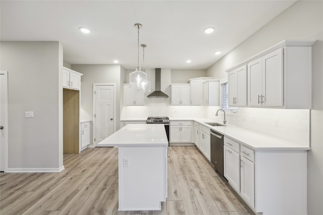 kitchen featuring appliances with stainless steel finishes, white cabinetry, sink, a center island, and wall chimney range hood