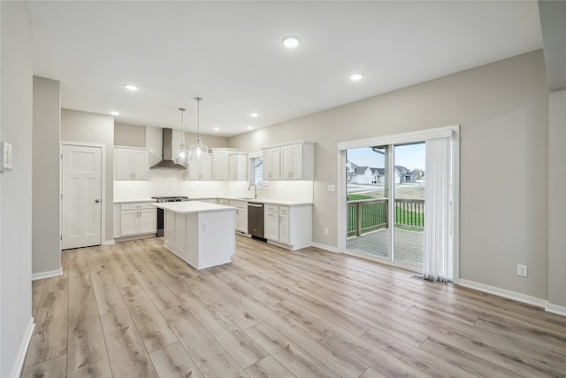 kitchen featuring decorative light fixtures, white cabinetry, a center island, stainless steel appliances, and wall chimney exhaust hood