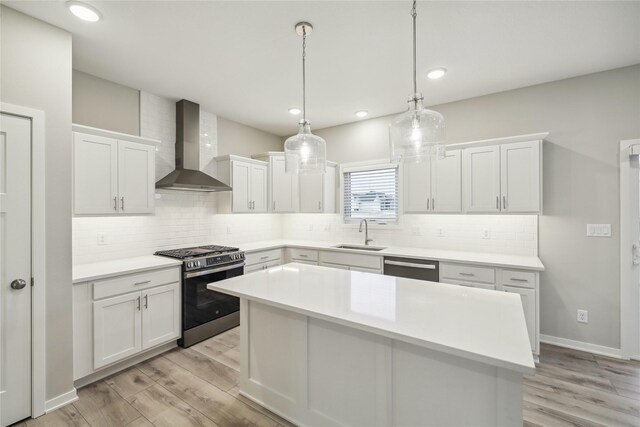kitchen featuring light wood-style floors, a sink, wall chimney range hood, and stainless steel appliances