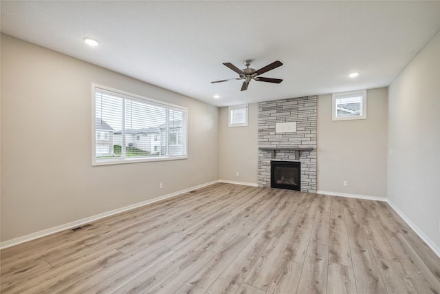 unfurnished living room featuring ceiling fan, plenty of natural light, a stone fireplace, and light wood-type flooring