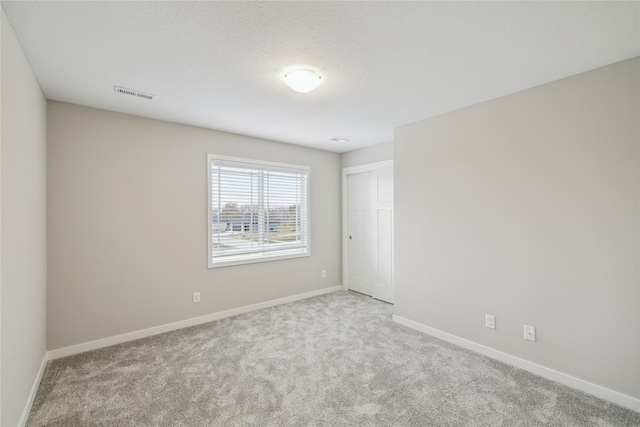 empty room with light colored carpet and a textured ceiling