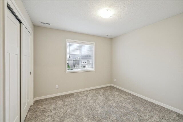 unfurnished bedroom featuring a textured ceiling, visible vents, baseboards, a closet, and carpet