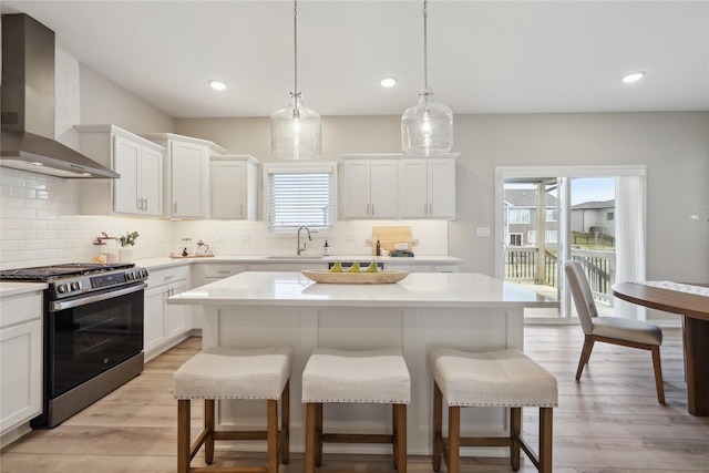 885 NW Frescott Cir, Waukee, IA 50263 - kitchen with gas stove, wall chimney range hood, a breakfast bar area, a sink, and recessed lighting