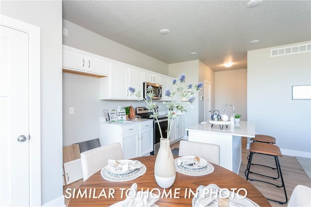 kitchen with stainless steel appliances, wood-type flooring, a textured ceiling, a center island with sink, and white cabinets