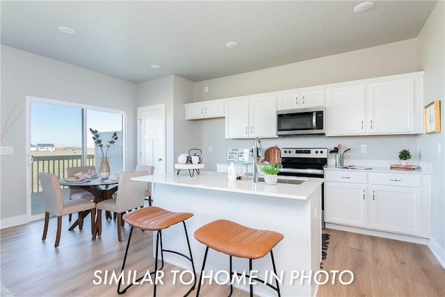 kitchen featuring white cabinetry, a kitchen island with sink, a breakfast bar, appliances with stainless steel finishes, and light wood-type flooring