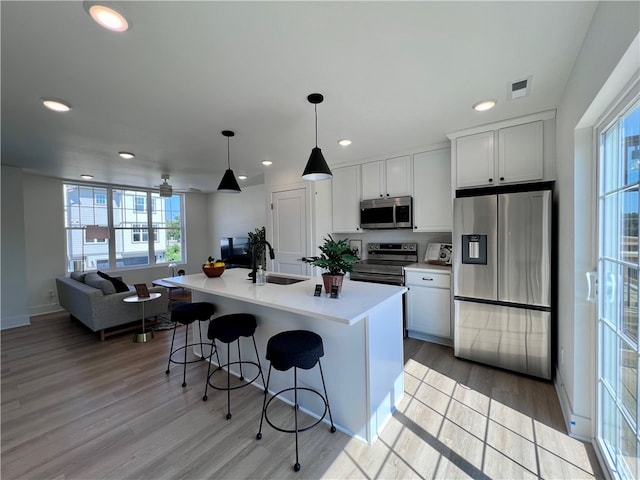 kitchen featuring a kitchen island with sink, decorative light fixtures, sink, appliances with stainless steel finishes, and white cabinets