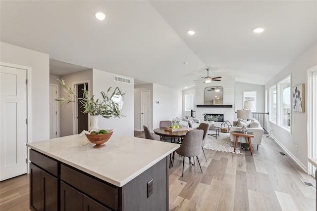 kitchen featuring a large fireplace, dark brown cabinetry, vaulted ceiling, ceiling fan, and light hardwood / wood-style flooring