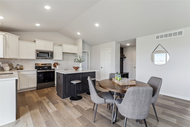 dining area featuring vaulted ceiling, light hardwood / wood-style flooring, and sink