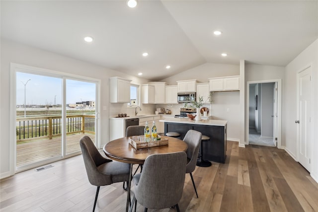 dining space with light hardwood / wood-style floors, lofted ceiling, and sink