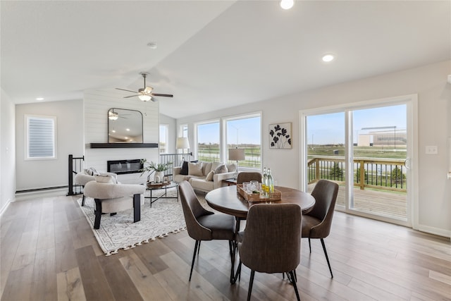 dining space featuring ceiling fan, light hardwood / wood-style flooring, a fireplace, and vaulted ceiling