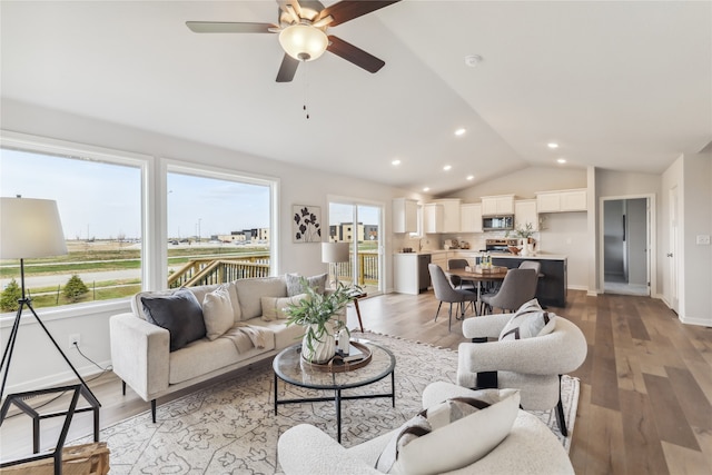 living room with ceiling fan, sink, vaulted ceiling, and light wood-type flooring