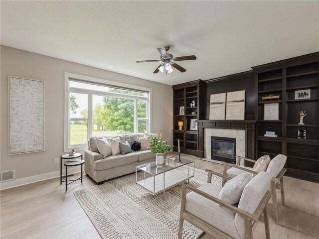 living room with ceiling fan, a fireplace, and light hardwood / wood-style flooring